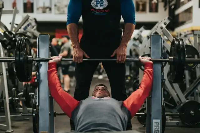 Man bench pressing a barbell with a spotter behind him