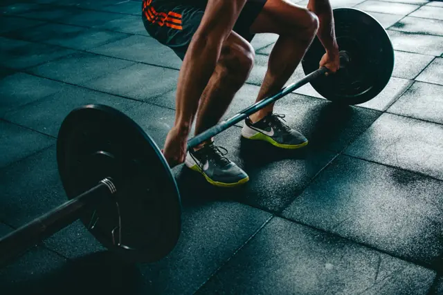 Lifter gripping a barbell on the gym floor for a deadlift