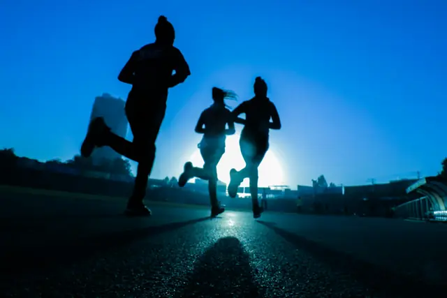 Three runners silhouetted against a blue evening sky